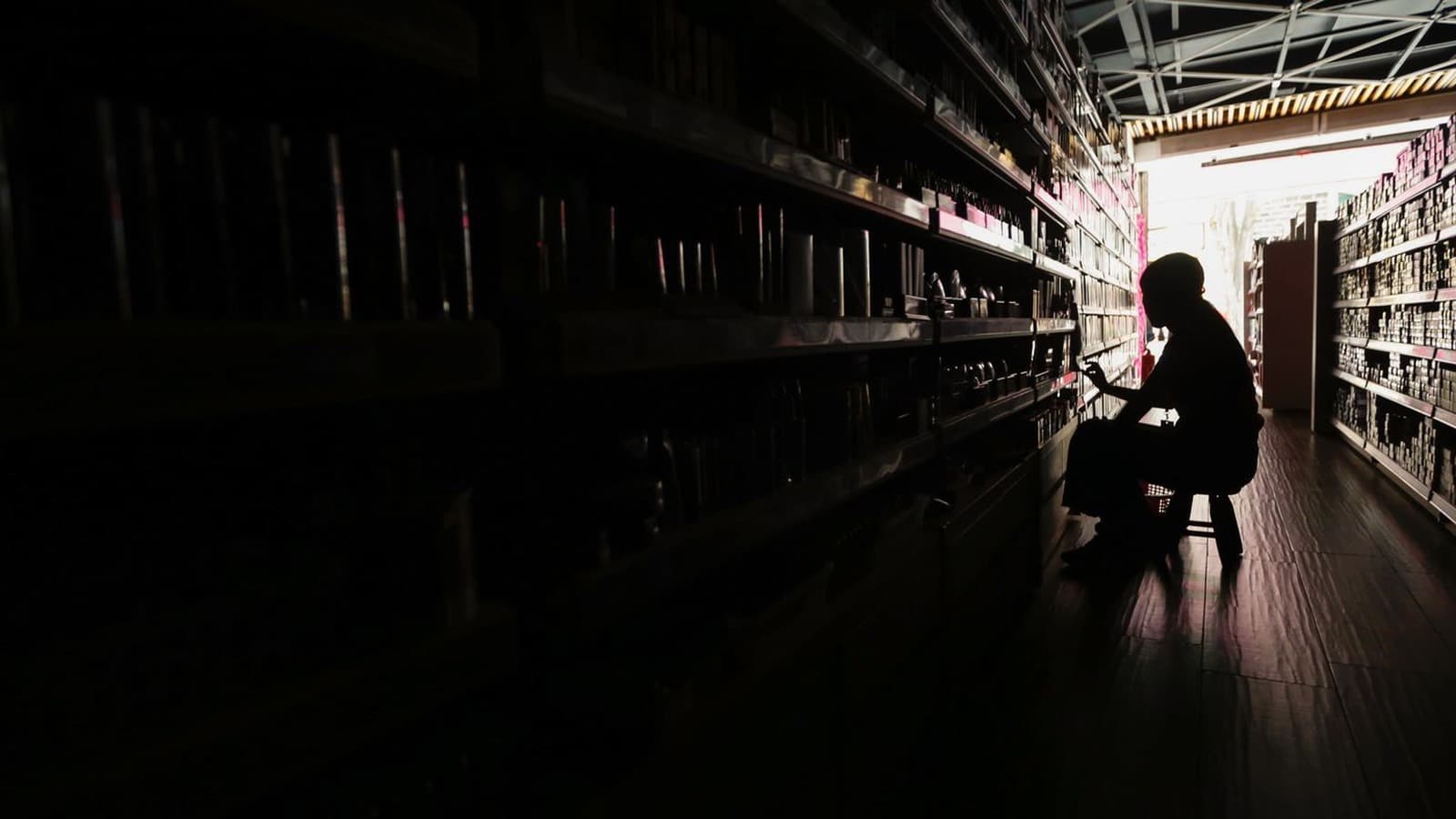 Interior de um comércio às escuras durante falta de luz, com a silhueta de uma pessoa junto às prateleiras; imagem de arquivo