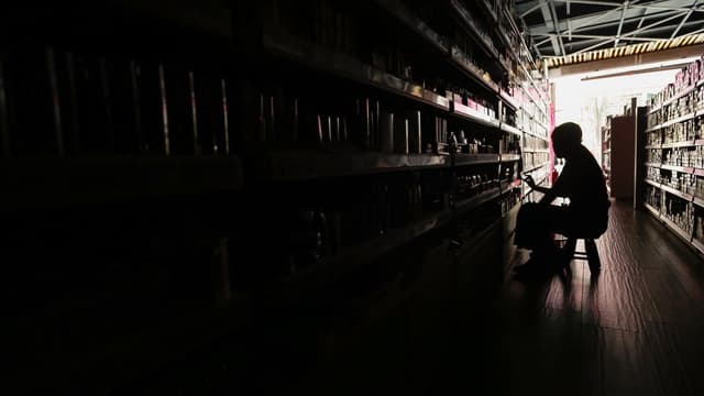 Interior de um comércio às escuras durante falta de luz, com a silhueta de uma pessoa junto às prateleiras; imagem de arquivo