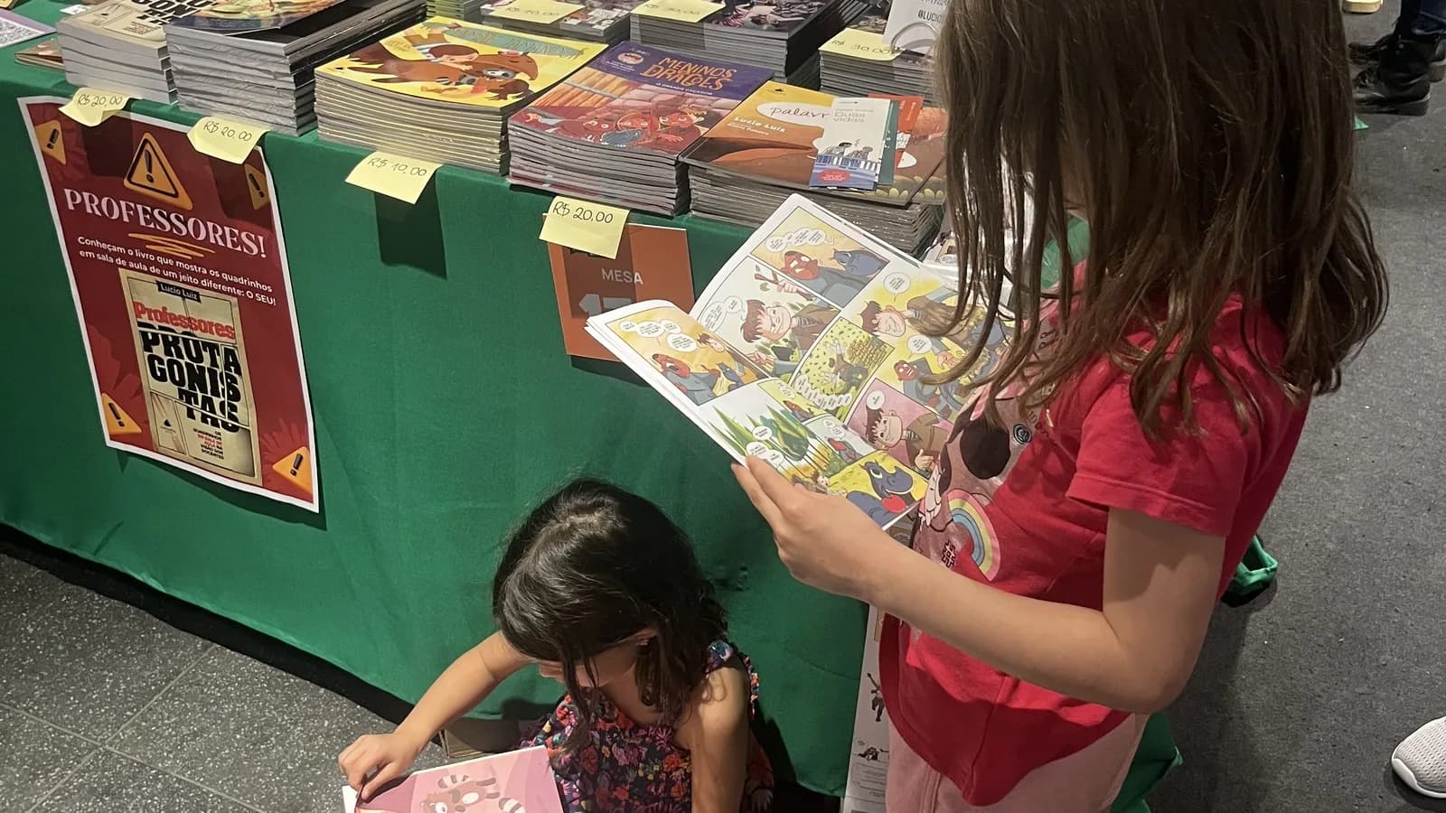 Duas crianças leem revistas em quadrinhos sentadas em evento literário
