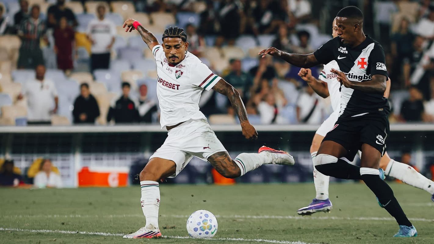 Jogador do Fluminense, de camisa branca com faixas verde e grená, finaliza a gol marcado por um atleta do Vasco, de camisa preta com faixa branca, no gramado do Maracanã