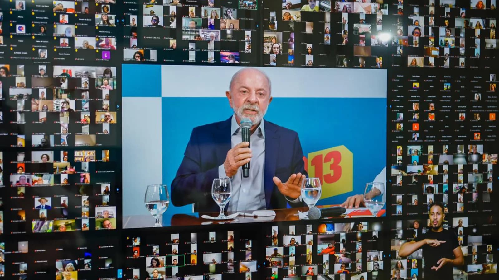 Lula durante transmissão ao vivo, com mosaico de espectadores ao fundo e placa com o número 13