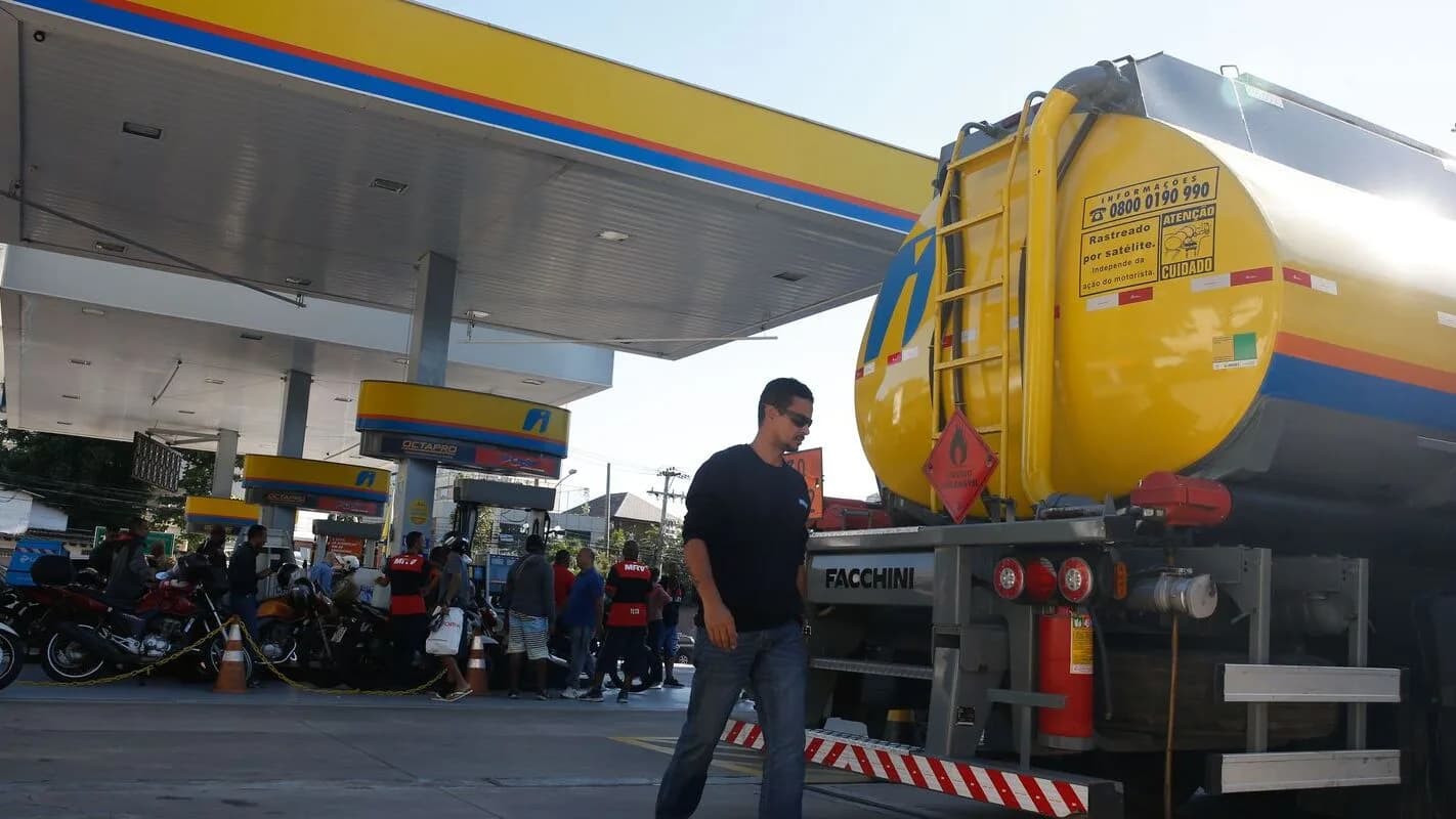 Caminhão-tanque abastecendo posto de combustível, com funcionário ao lado