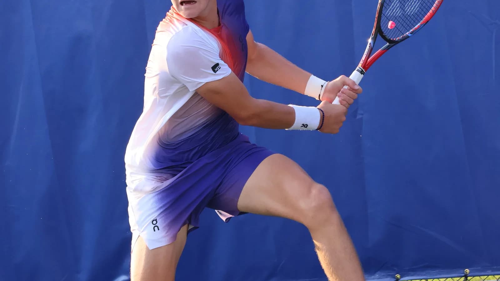 João Fonseca em quadra durante partida de tênis, preparando um golpe de backhand