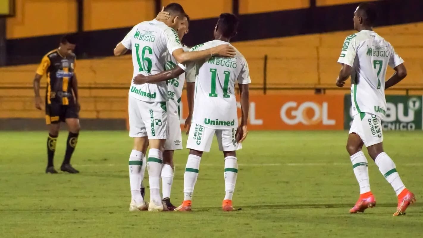 Jogadores da Chapecoense em uniforme branco se abraçam em comemoração durante partida de futebol