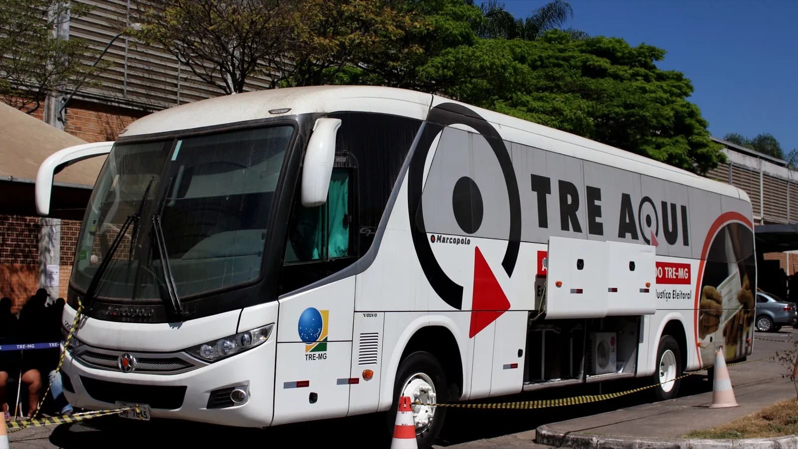 Ônibus itinerante do TRE-MG estacionado em via pública, com a inscrição "TRE Aqui" e o brasão da Justiça Eleitoral