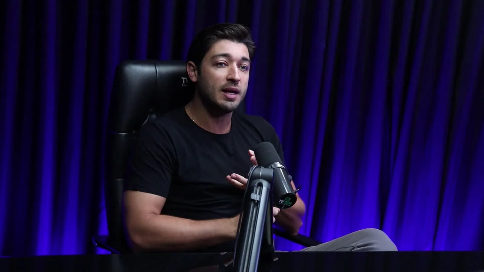 Rafael, fundador da Hoomy, gesticula durante entrevista sentado em cadeira gamer, diante de cortina azul