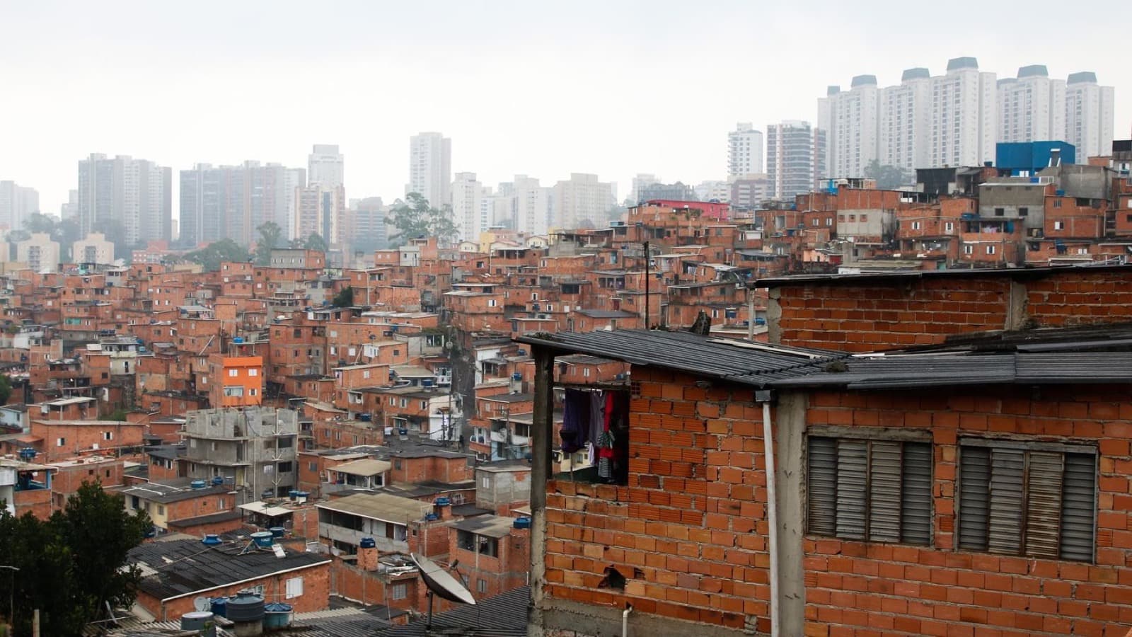 Vista da comunidade de Paraisópolis, com casas de alvenaria sem reboco e prédios altos do Morumbi ao fundo, em São Paulo; imagem de arquivo