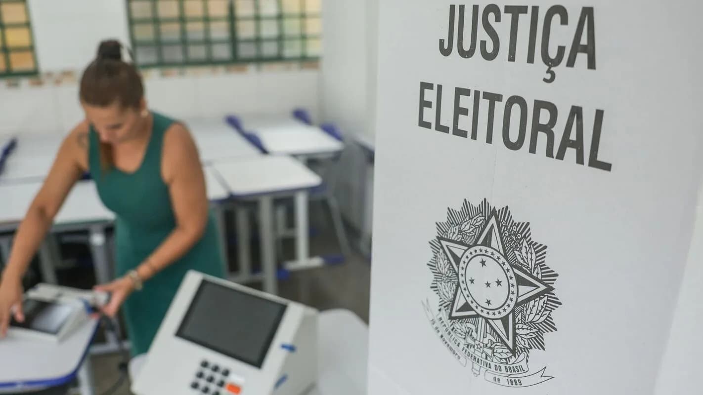 Eleitora vota em urna eletrônica ao lado de placa da Justiça Eleitoral