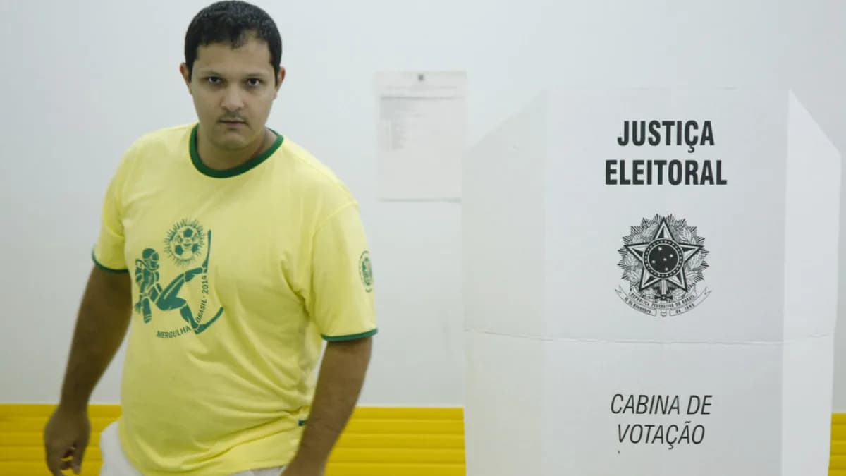 Eleitor com camisa verde-amarela caminha para a cabine de votação, sob placa da Justiça Eleitoral