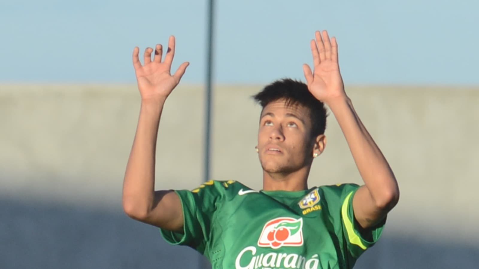 Neymar, de camisa de treino verde da seleção brasileira com o escudo da CBF, com os braços erguidos e o olhar voltado para cima durante treino, em imagem de arquivo de 2013