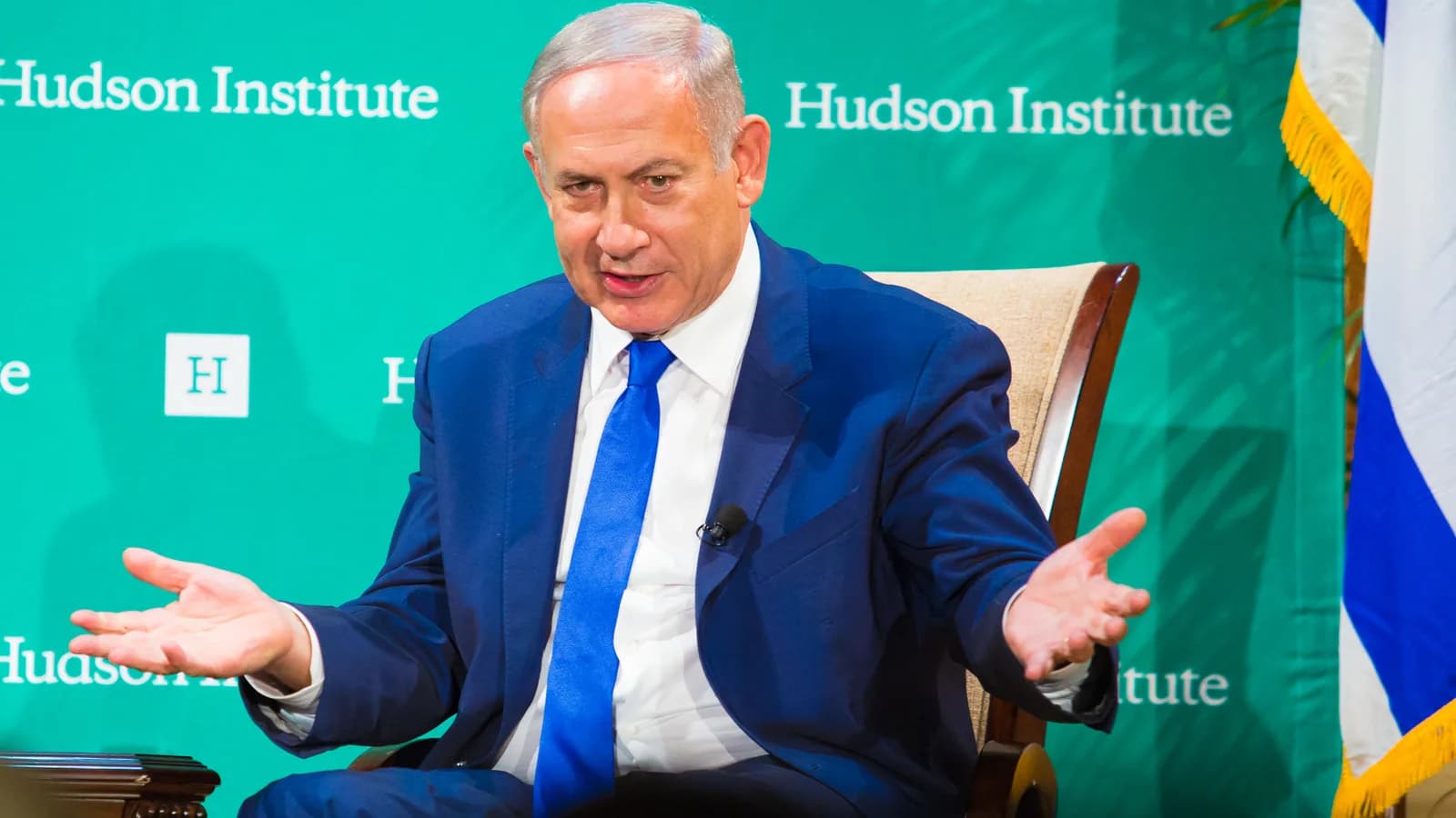 Benjamin Netanyahu gesticula durante entrevista, com bandeira de Israel ao fundo