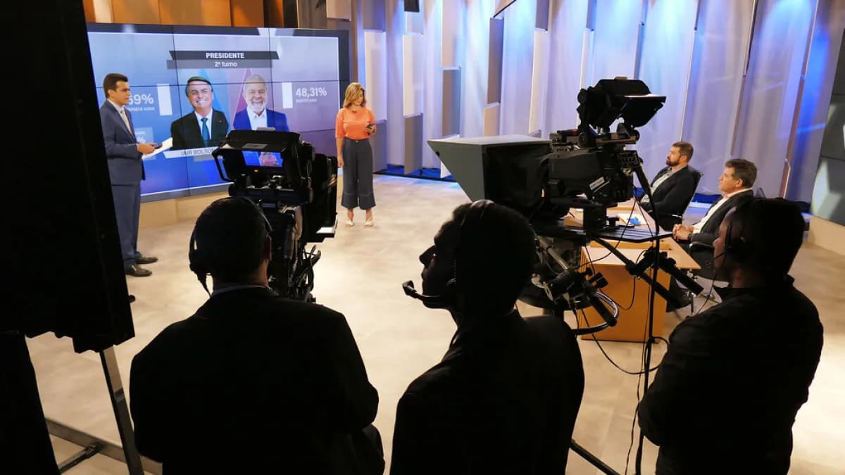 Estúdio de TV com equipe de produção acompanhando telão de resultados eleitorais