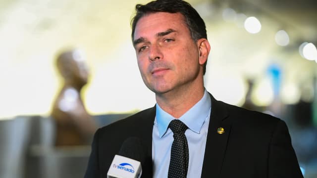 O senador Flávio Bolsonaro fala a jornalistas cercado de microfones em entrevista coletiva