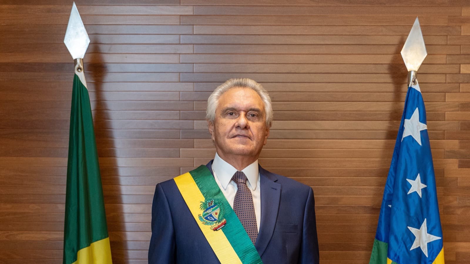 O governador Ronaldo Caiado, de terno azul e faixa de governador de Goiás, ao lado das bandeiras do Brasil e de Goiás, em foto de arquivo de 2023