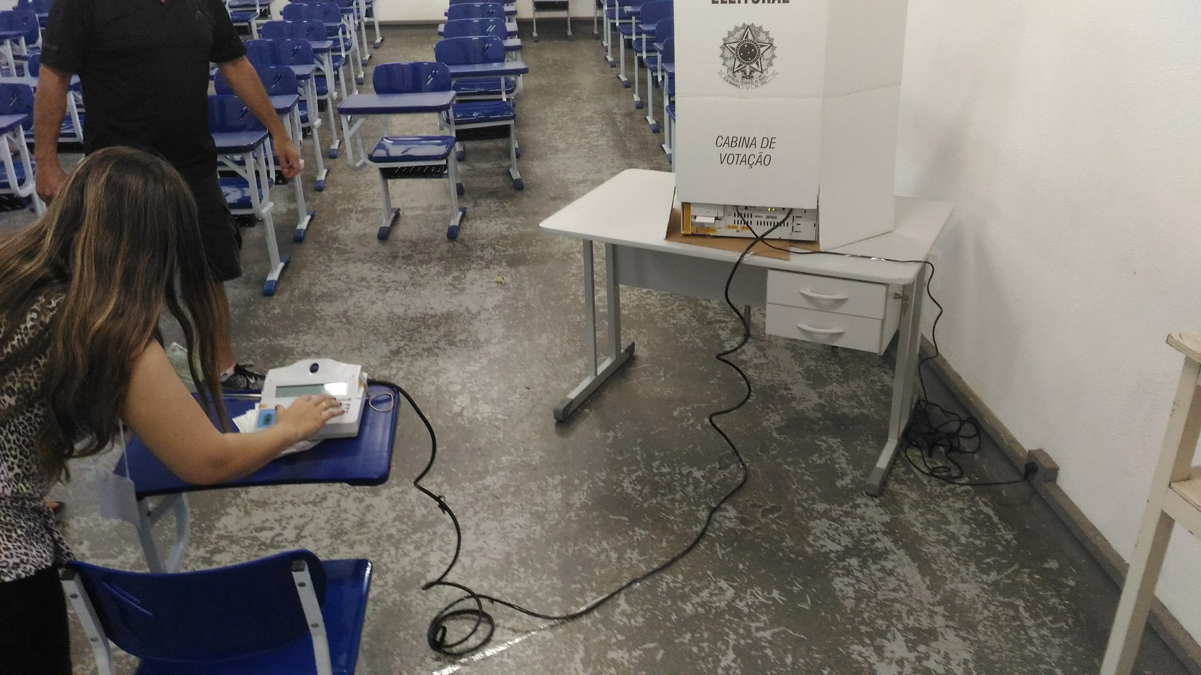 Mesária opera terminal eleitoral ao lado da cabina de votação (imagem de arquivo de eleição municipal em Itajubá, MG, ilustrativa do uso da urna eletrônica)