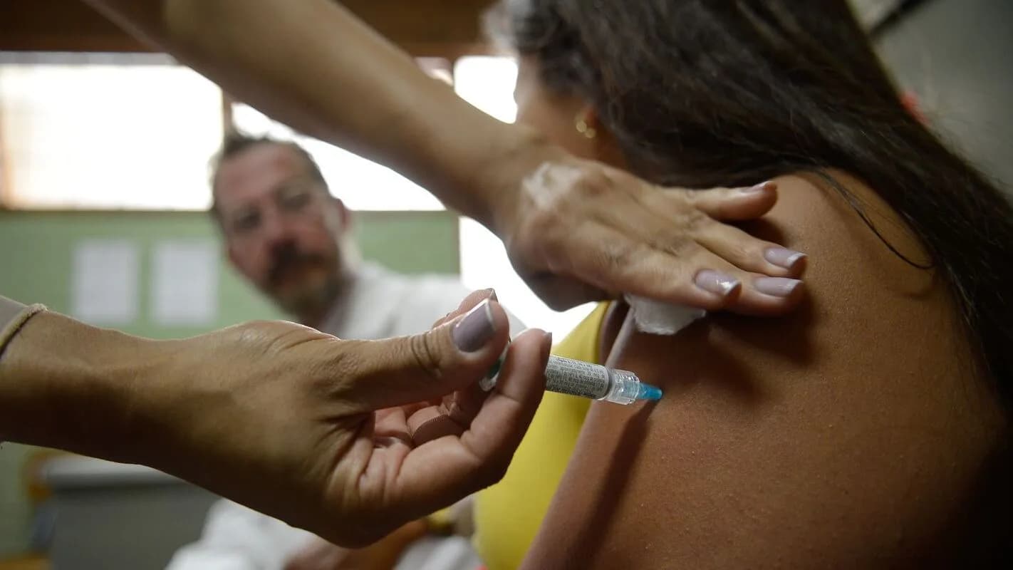 Profissional de saúde aplica vacina no braço de uma paciente em posto de saúde