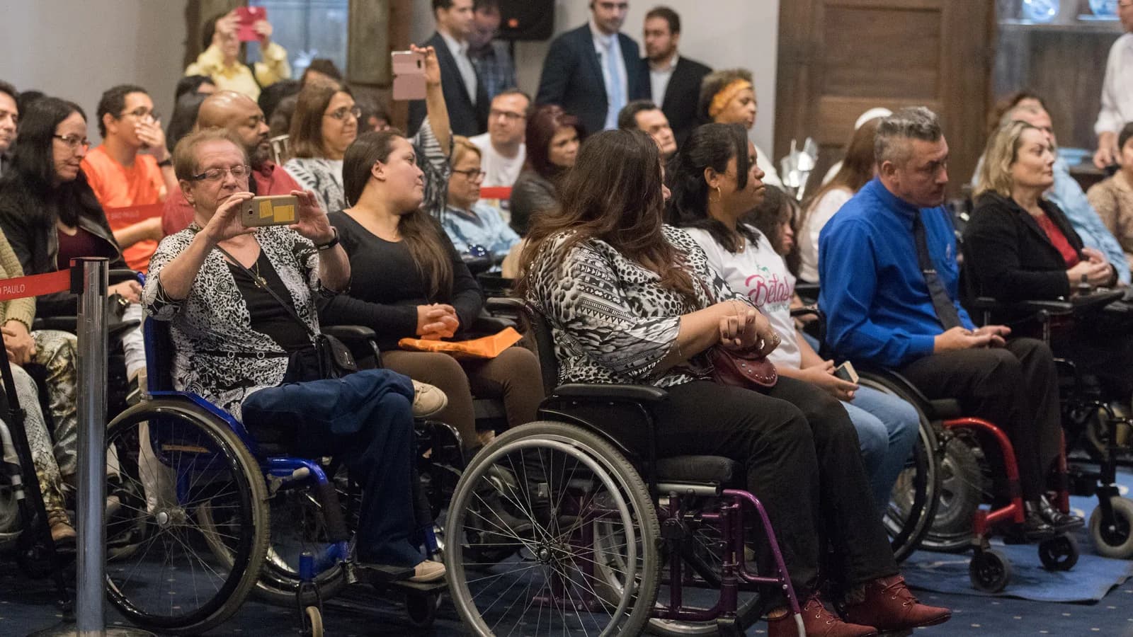 Pessoas com deficiência, várias em cadeira de rodas, reunidas em evento público