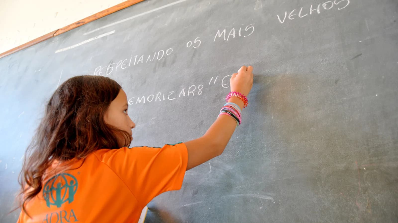 Criança escreve na lousa em sala de aula durante atividade de alfabetização