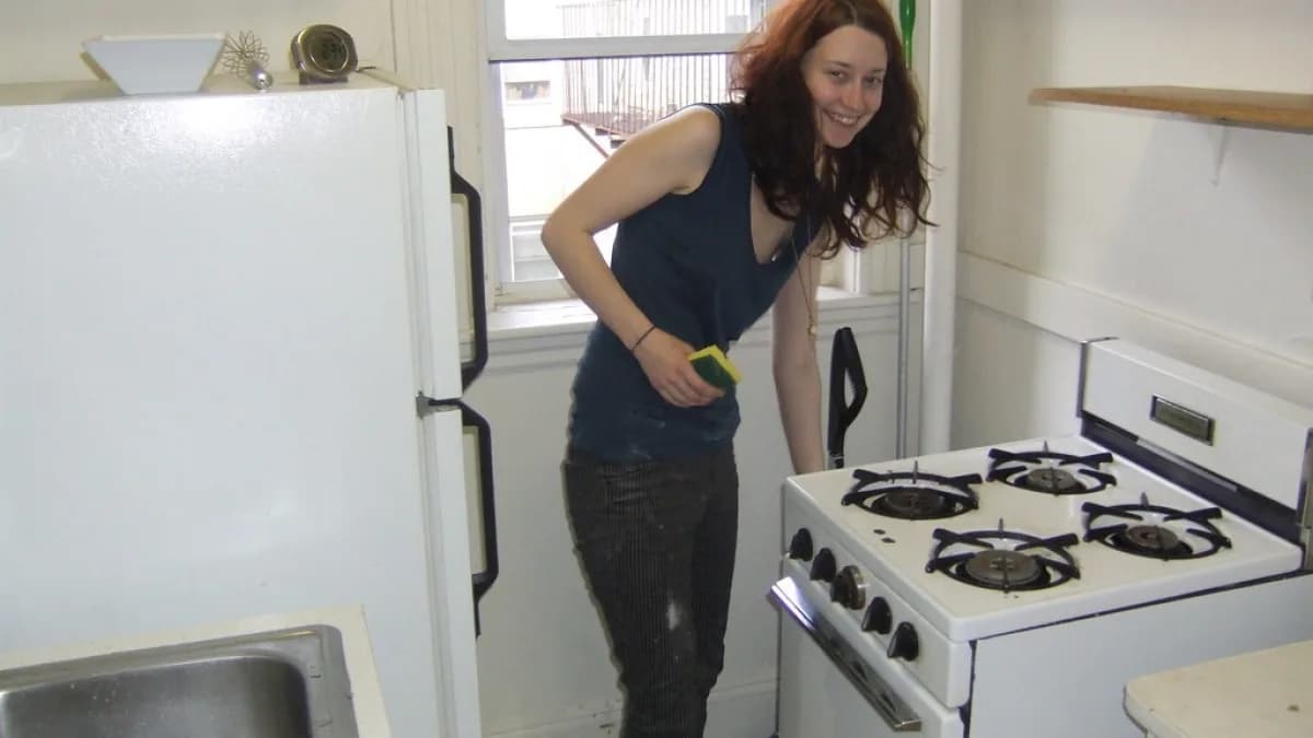 Mulher limpa fogão na cozinha de casa com produto de limpeza