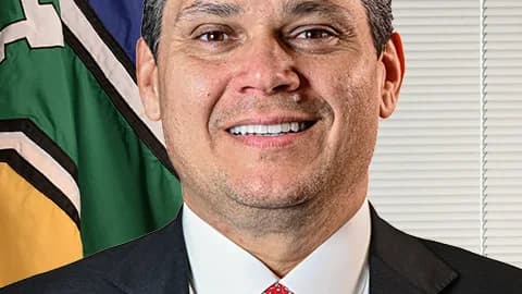 Davi Alcolumbre sorri em retrato oficial, com bandeira do Amapá ao fundo