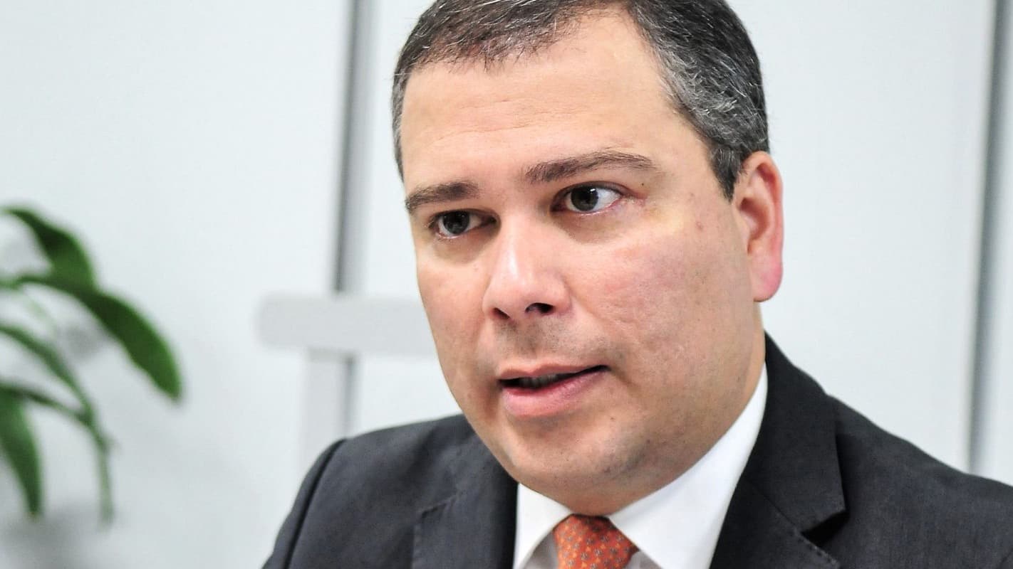 Paulo Henrique Costa, ex-presidente do BRB, fala em entrevista vestindo terno escuro e gravata laranja