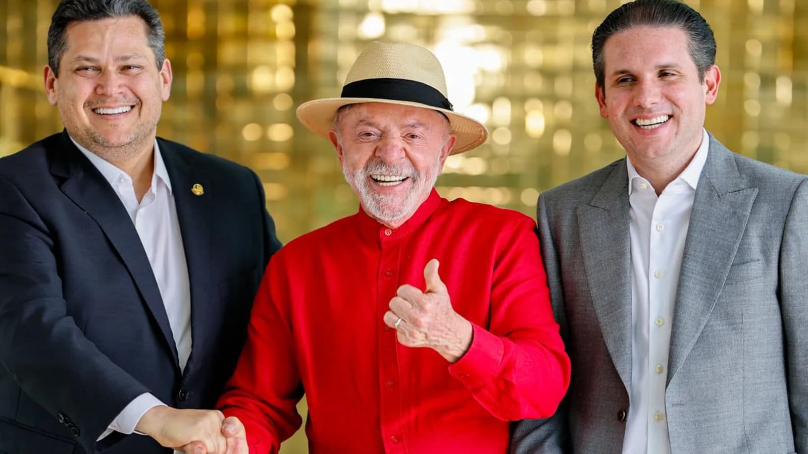 Lula, de camisa vermelha, ao lado de Davi Alcolumbre e Hugo Motta, sorrindo em corredor do Planalto
