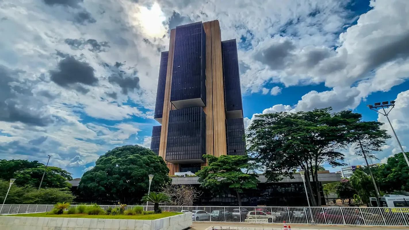 Fachada da sede do Banco Central do Brasil em Brasília, prédio revestido em vidro escuro e ripas douradas, sob céu com nuvens