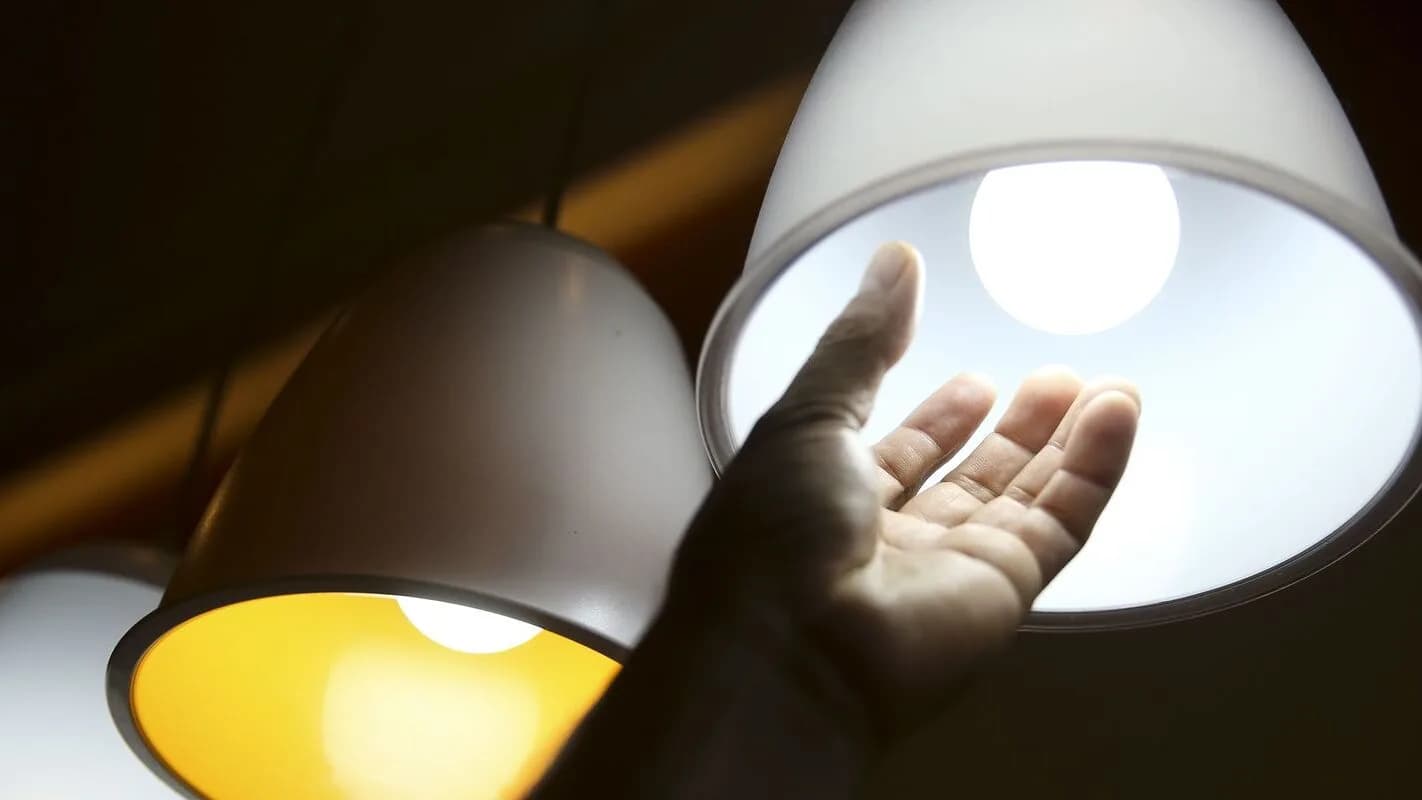 Mão próxima a lâmpadas acesas, ilustrando o consumo de energia elétrica (imagem de arquivo)