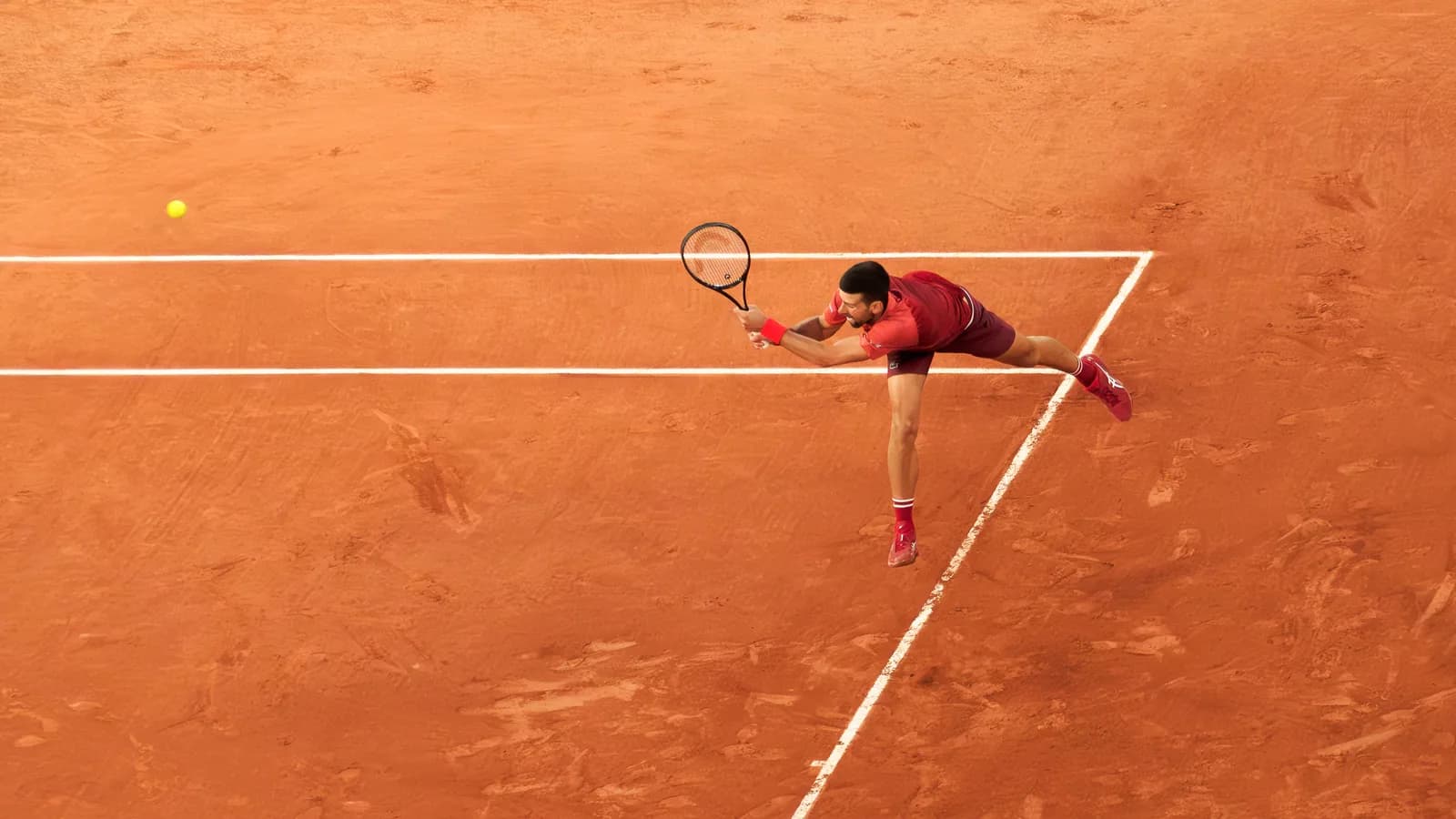 Novak Djokovic se estica para alcançar a bola durante partida de tênis em quadra de saibro