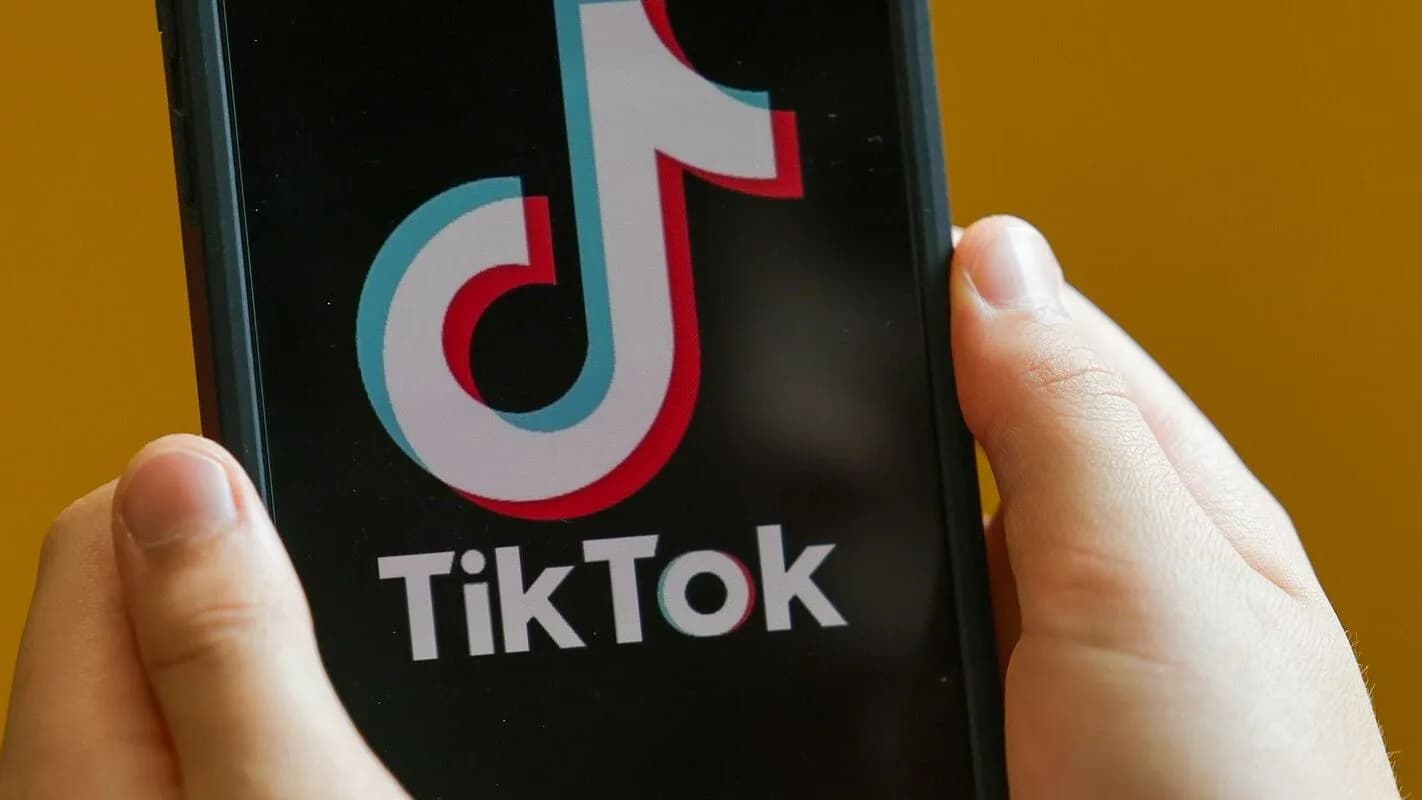 Mãos seguram um celular com o aplicativo TikTok aberto na tela
