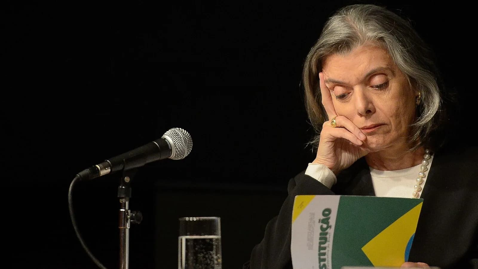 Ministra Cármen Lúcia lê um exemplar da Constituição durante evento, com microfone à frente