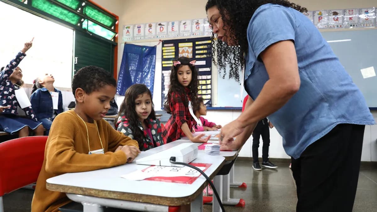 Urna eletrônica apresentada por representante do TSE durante feira de ciências em escola, com crianças observando