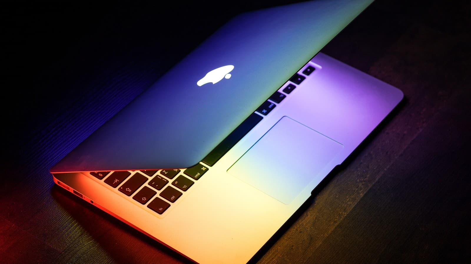 MacBook Air de 2015 semiaberto sobre mesa de madeira, iluminado por luzes coloridas