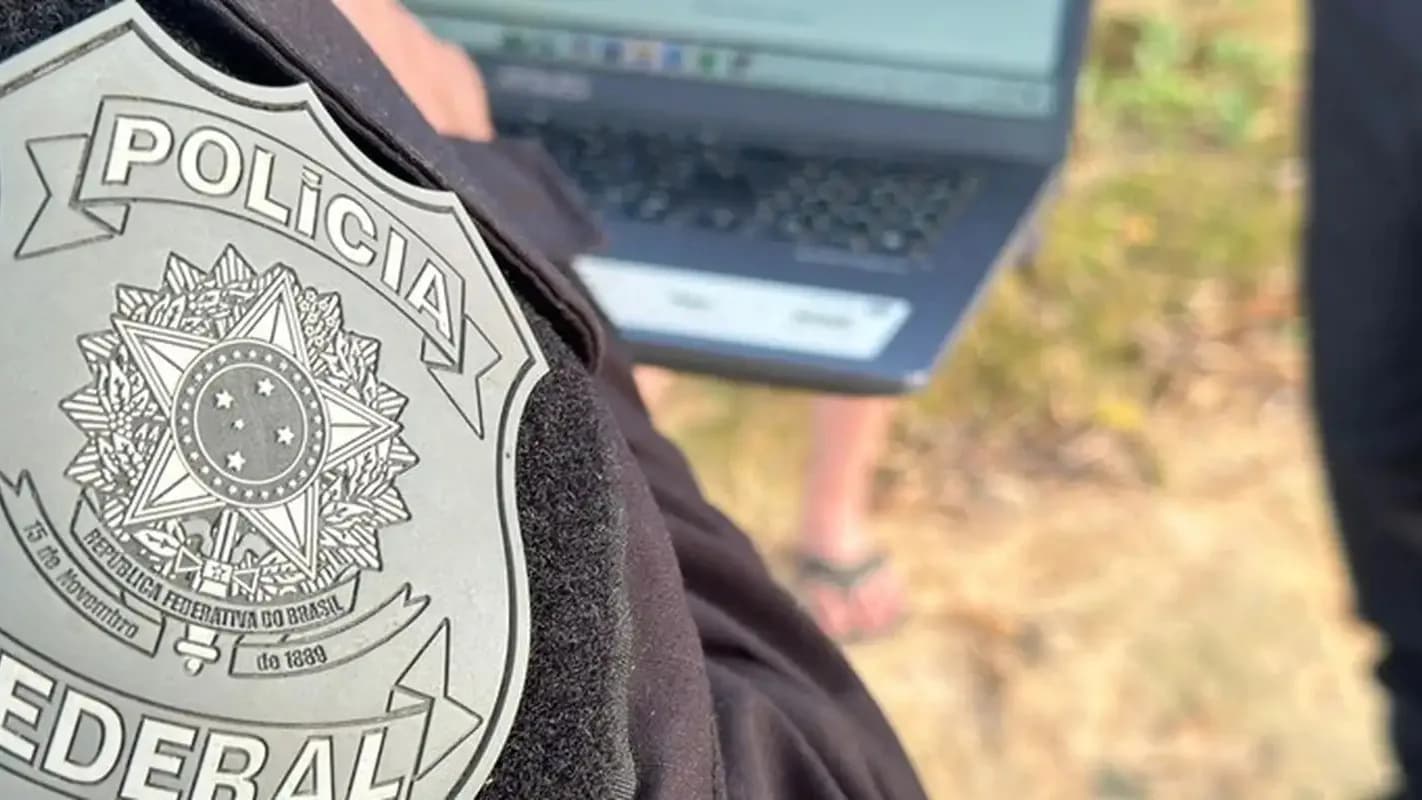 Distintivo da Polícia Federal em destaque, com agente ao fundo