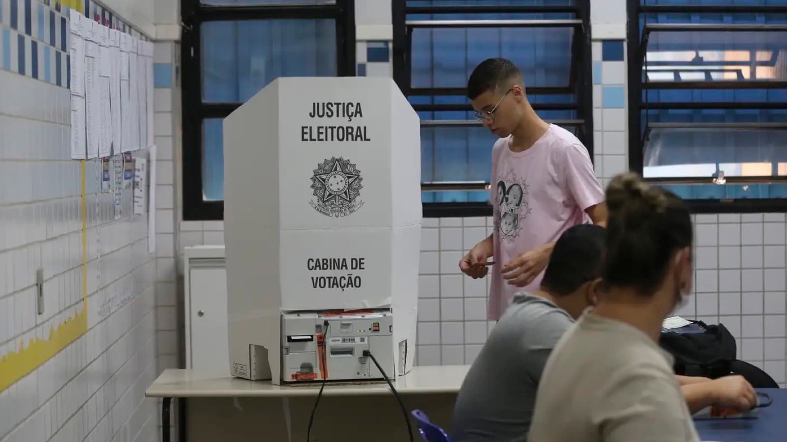 Cabina de votação da Justiça Eleitoral com eleitor se aproximando da urna eletrônica, foto de arquivo