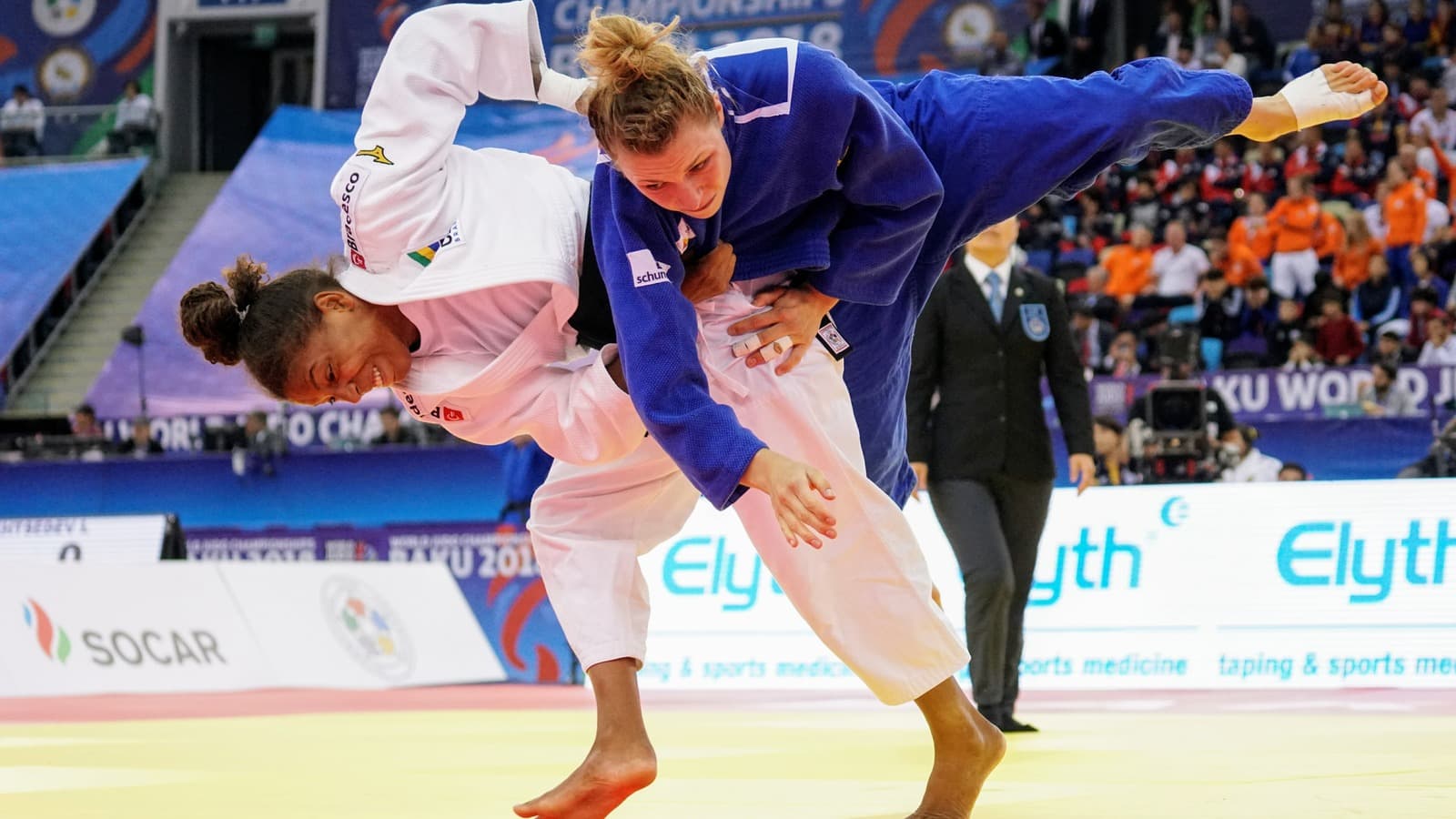 A judoca brasileira Rafaela Silva, de quimono branco, aplica um golpe em adversária de quimono azul durante disputa de equipes mistas; imagem de arquivo do Mundial de Judô de Baku, em 2018