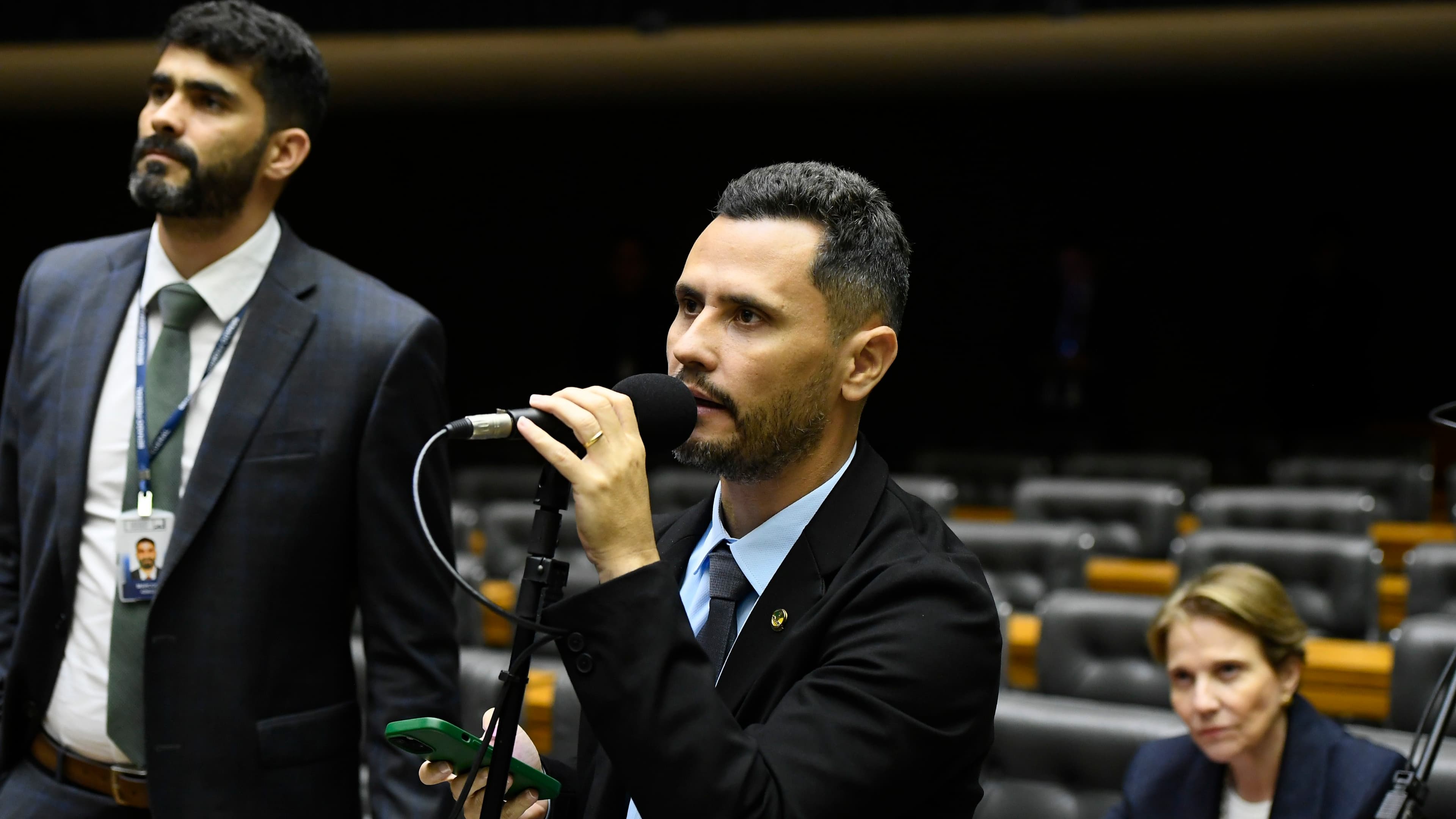 Parlamentar fala ao microfone no plenário em sessão anterior do Congresso Nacional, com fileiras de cadeiras vazias ao fundo