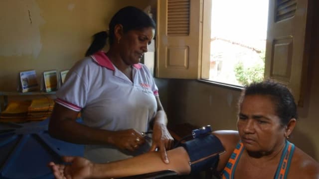 Profissional de saúde mede a pressão arterial de uma paciente em consulta