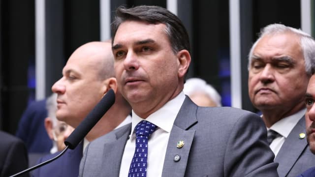 O senador Flávio Bolsonaro fala ao microfone durante sessão do Congresso Nacional, ao lado de outros parlamentares