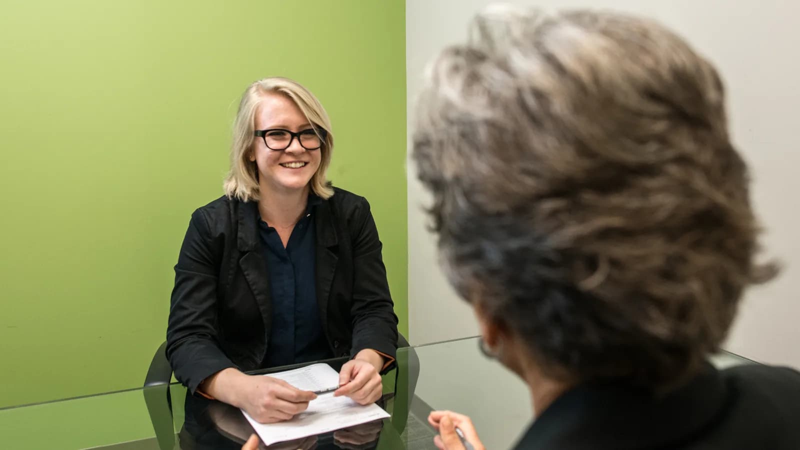 Mulher participa de entrevista de emprego sentada à mesa com entrevistadora