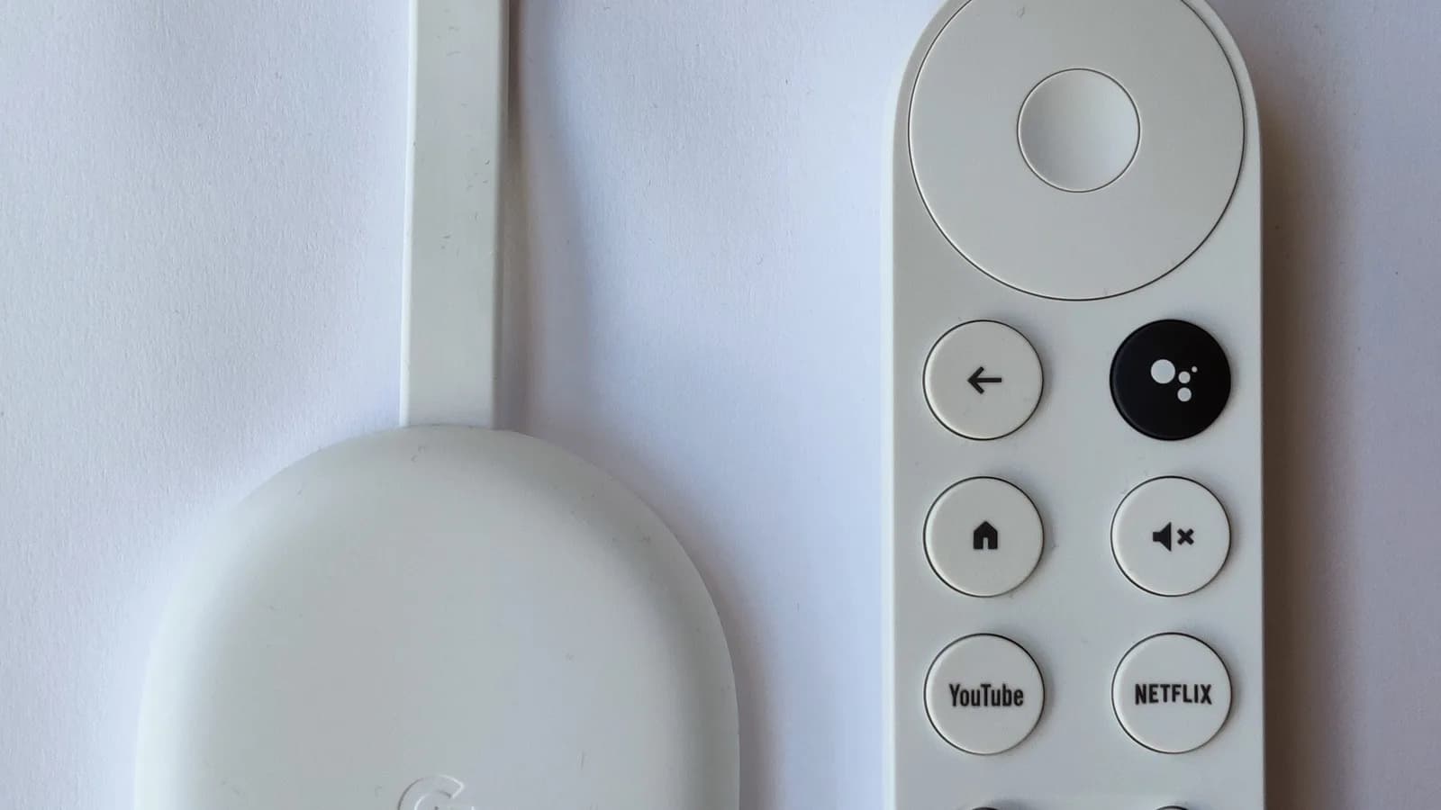Controle remoto do Google TV ao lado de um Chromecast, com botão de mute visível