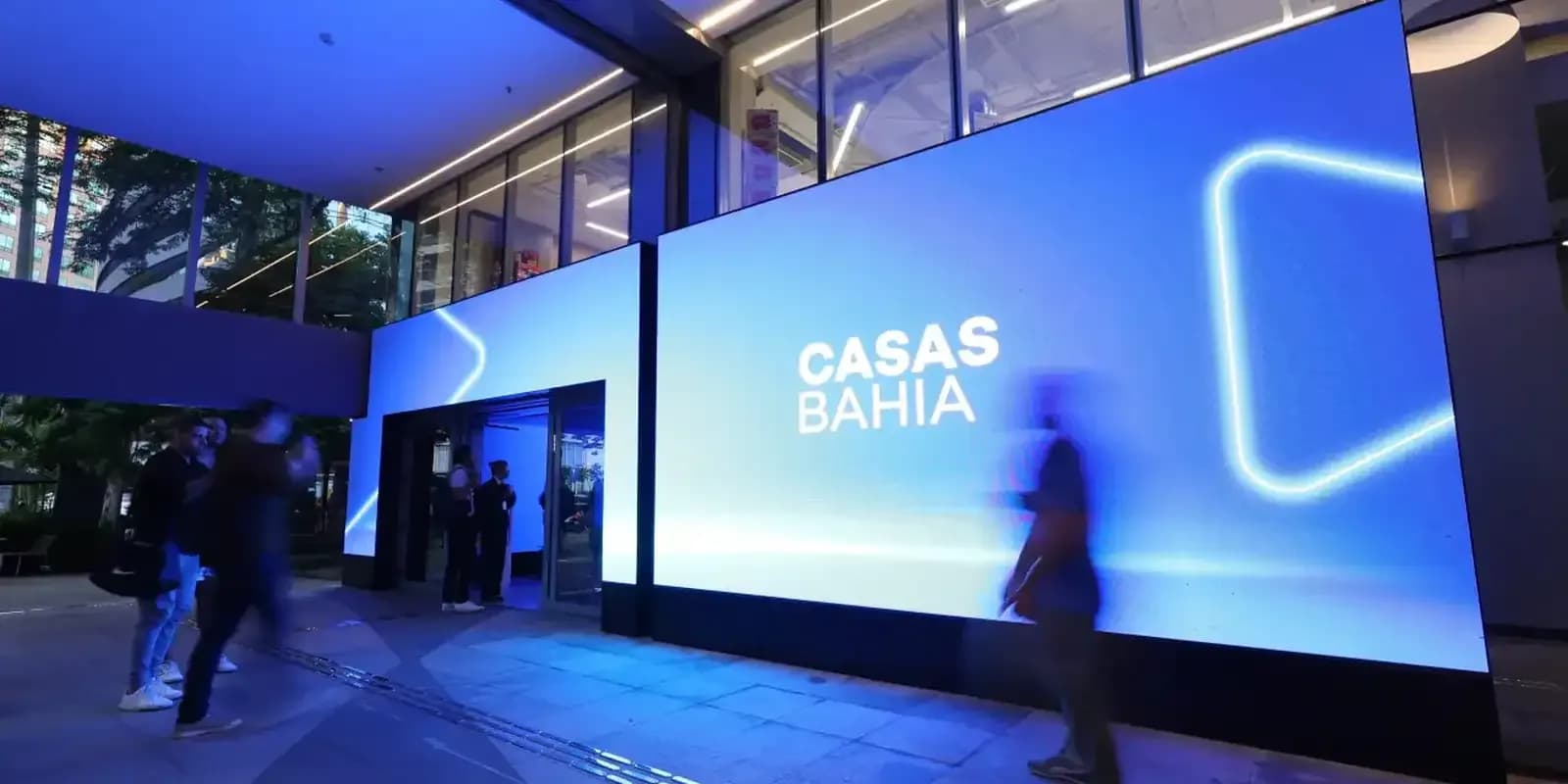 Fachada iluminada da sede da Casas Bahia, com pessoas entrando no prédio à noite
