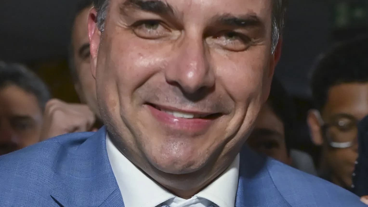 O senador Flávio Bolsonaro sorri durante entrevista cercado por microfones