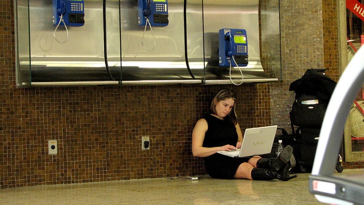 Pessoa sentada no chão usa notebook em espaço público