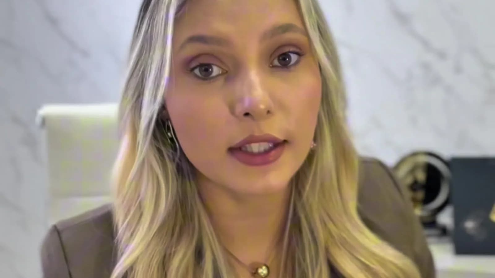 A advogada Isabela Costa fala em vídeo, com um fundo de mármore e uma legenda mostrando seu nome e a profissão.