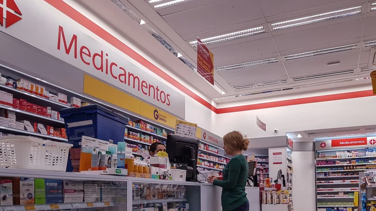 Interior de farmácia com cliente e prateleiras de medicamentos