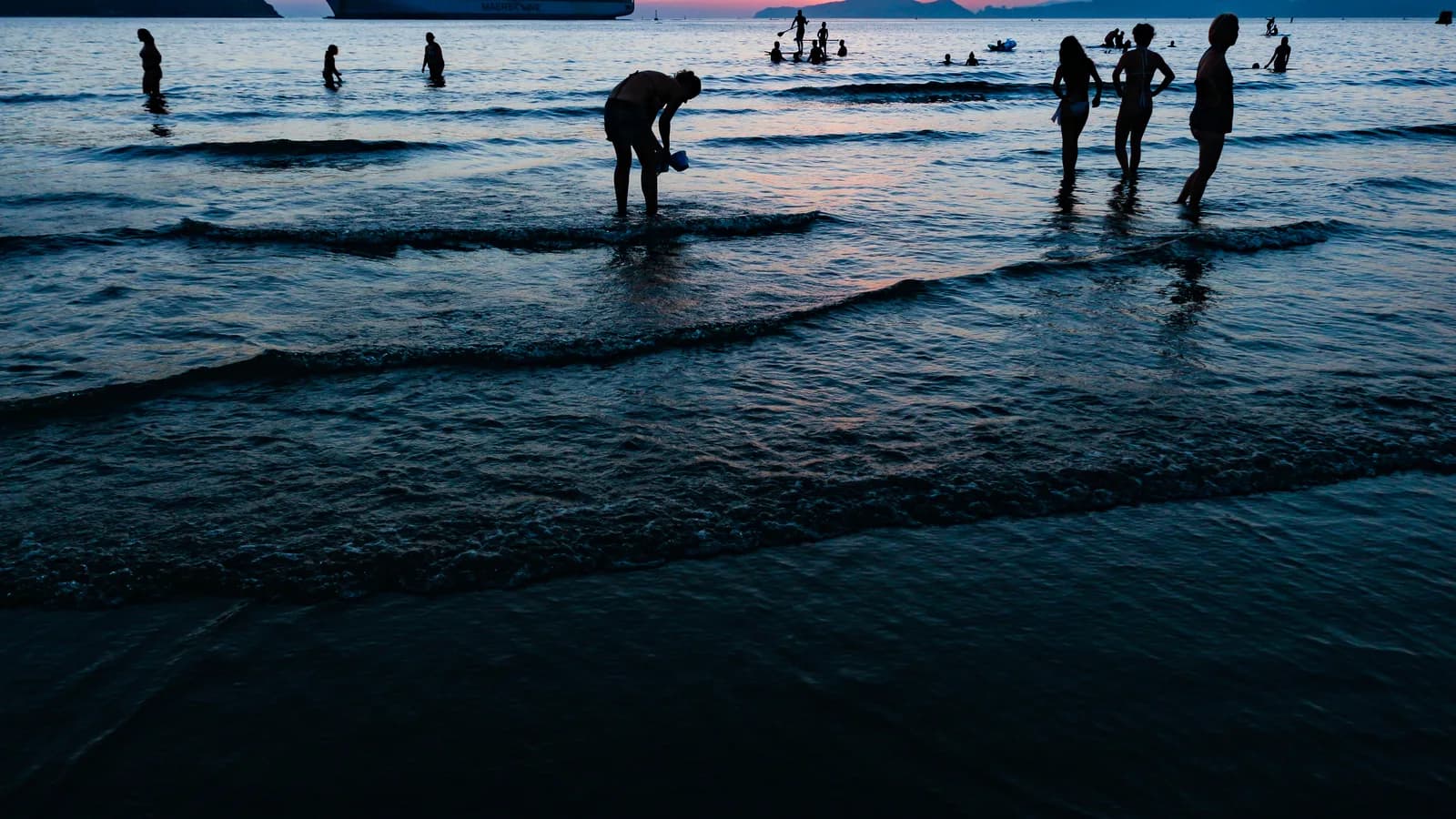 Banhistas na praia de Santos (SP) ao entardecer, com navio ao fundo