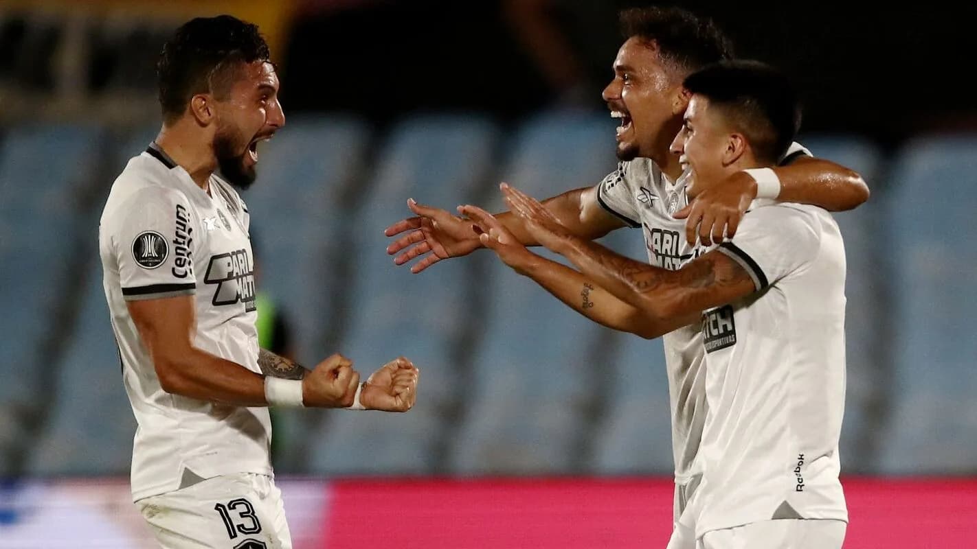 Jogadores do Botafogo comemorando gol em campo, uniforme branco com detalhes pretos