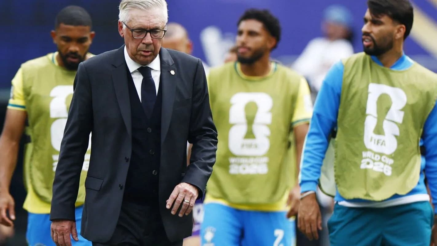 Carlo Ancelotti caminha de terno ao lado de jogadores da Seleção Brasileira com coletes da Copa do Mundo 2026