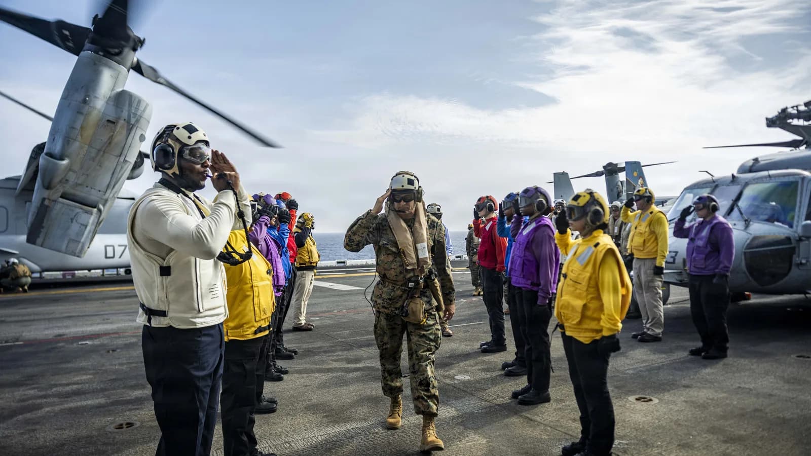 Marinheiros perfilados no convés de um navio de guerra dos EUA fazem continência enquanto um militar caminha entre eles